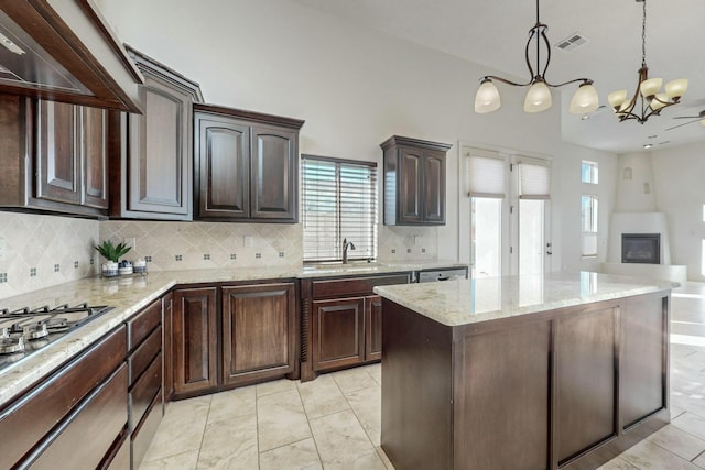 kitchen with visible vents, a glass covered fireplace, an inviting chandelier, wall chimney range hood, and a sink