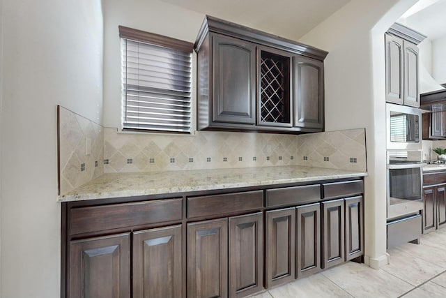 kitchen featuring light stone counters, dark brown cabinets, appliances with stainless steel finishes, decorative backsplash, and a warming drawer