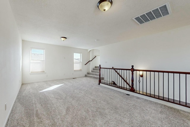 empty room featuring a textured ceiling, visible vents, baseboards, stairs, and carpet