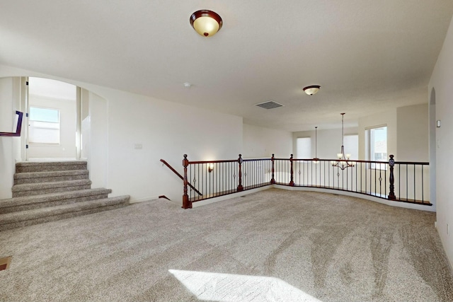 carpeted spare room with visible vents and a notable chandelier