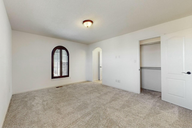 unfurnished bedroom with carpet floors, arched walkways, a closet, and visible vents