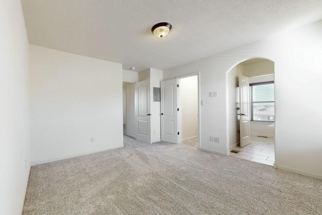 unfurnished bedroom with baseboards, carpet, arched walkways, and a textured ceiling