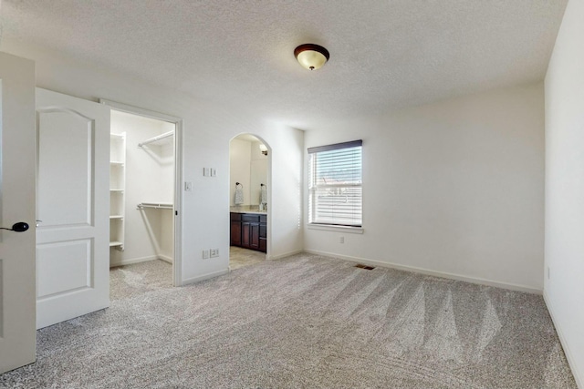 unfurnished bedroom with a textured ceiling, arched walkways, light carpet, a spacious closet, and a closet