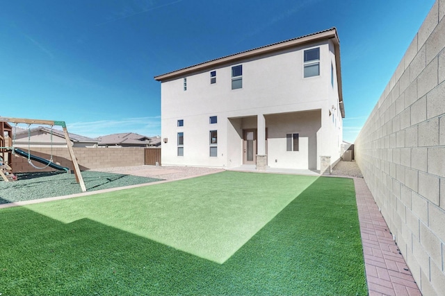 back of property with a lawn, a fenced backyard, a patio area, a playground, and stucco siding