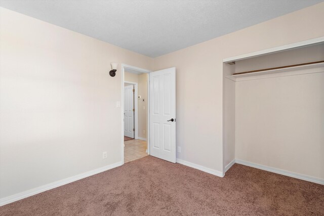 unfurnished bedroom featuring light carpet, a textured ceiling, and a closet