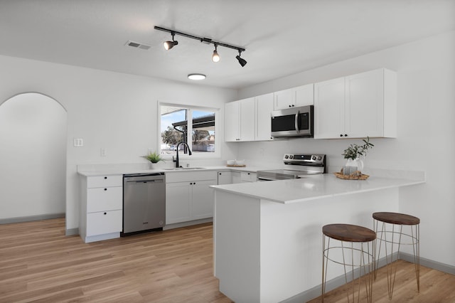 kitchen featuring sink, appliances with stainless steel finishes, white cabinetry, a kitchen breakfast bar, and kitchen peninsula