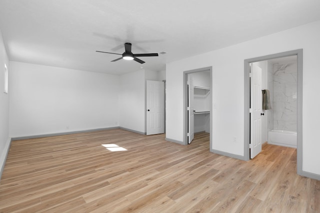 unfurnished bedroom with ensuite bathroom, a walk in closet, ceiling fan, light wood-type flooring, and a closet