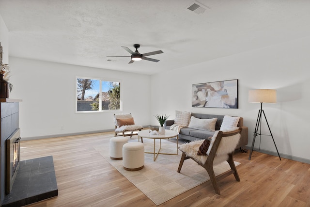 living room with ceiling fan, a tiled fireplace, and light hardwood / wood-style floors