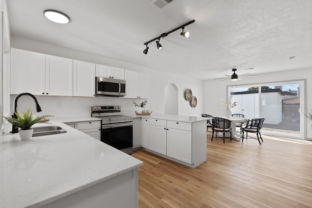 kitchen with appliances with stainless steel finishes, kitchen peninsula, sink, and white cabinets