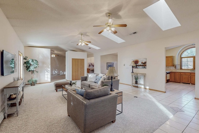 tiled living room with ceiling fan, a textured ceiling, and vaulted ceiling with skylight