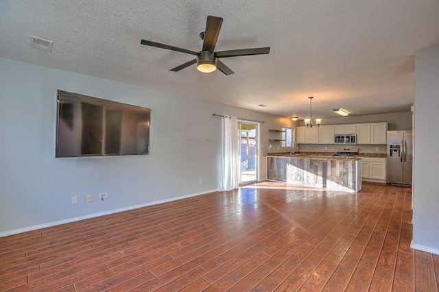 unfurnished living room with dark wood-type flooring, sink, ceiling fan with notable chandelier, and a textured ceiling