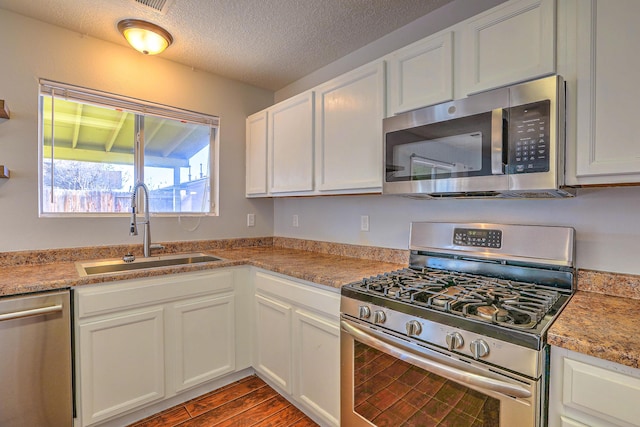 kitchen featuring appliances with stainless steel finishes, hardwood / wood-style floors, sink, white cabinets, and a textured ceiling