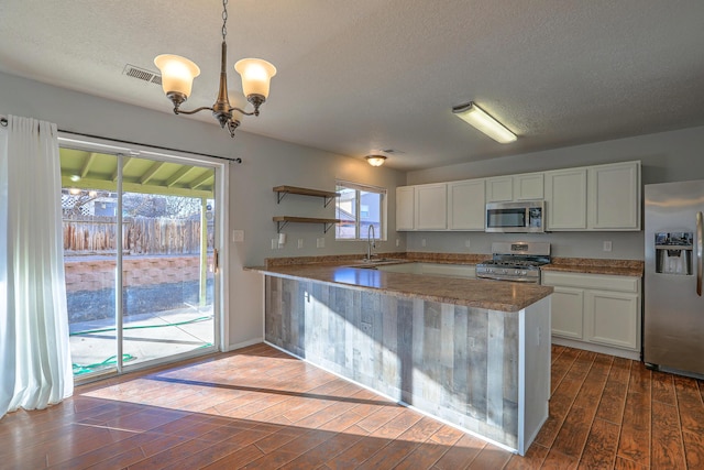 kitchen with sink, dark wood-type flooring, stainless steel appliances, white cabinets, and decorative light fixtures