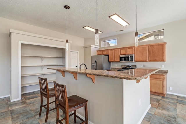 kitchen with a breakfast bar area, stone counters, appliances with stainless steel finishes, a textured ceiling, and decorative light fixtures