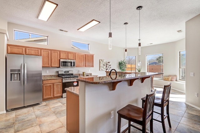 kitchen featuring appliances with stainless steel finishes, hanging light fixtures, a kitchen bar, a center island with sink, and dark stone counters