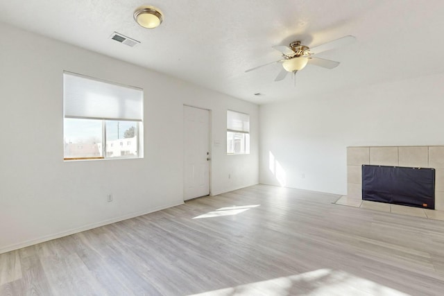 unfurnished living room featuring a fireplace, plenty of natural light, ceiling fan, and light wood-type flooring