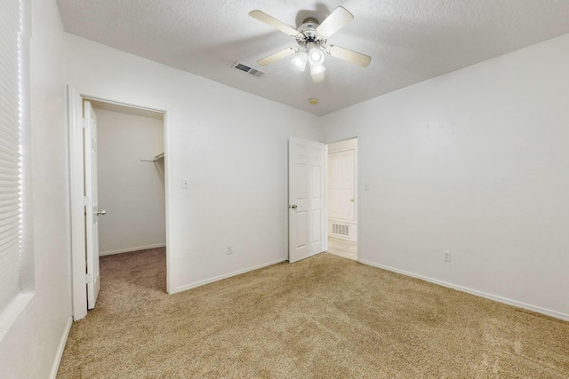 unfurnished bedroom with a walk in closet, light colored carpet, a textured ceiling, a closet, and ceiling fan