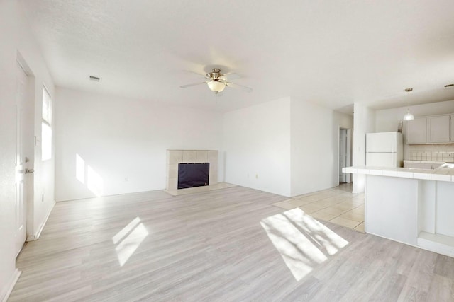 unfurnished living room with a tile fireplace, ceiling fan, and light wood-type flooring