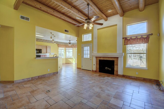 unfurnished living room with wood ceiling, a tile fireplace, ceiling fan, beam ceiling, and a towering ceiling