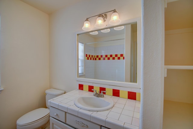 bathroom with vanity, backsplash, toilet, and tiled shower