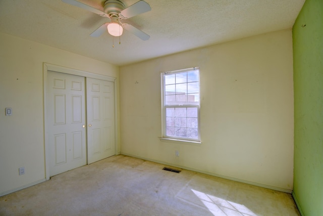 unfurnished bedroom featuring ceiling fan, a textured ceiling, light carpet, and a closet