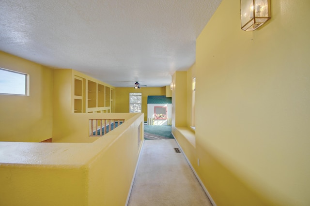 hallway with light colored carpet and a textured ceiling