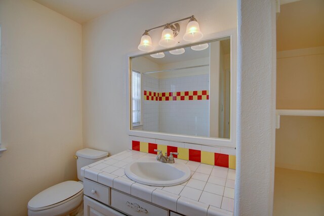 bathroom with vanity, tasteful backsplash, tiled shower, and toilet