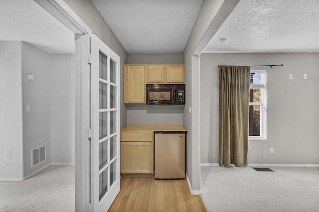 kitchen featuring light colored carpet, stainless steel fridge, light brown cabinetry, and a textured ceiling