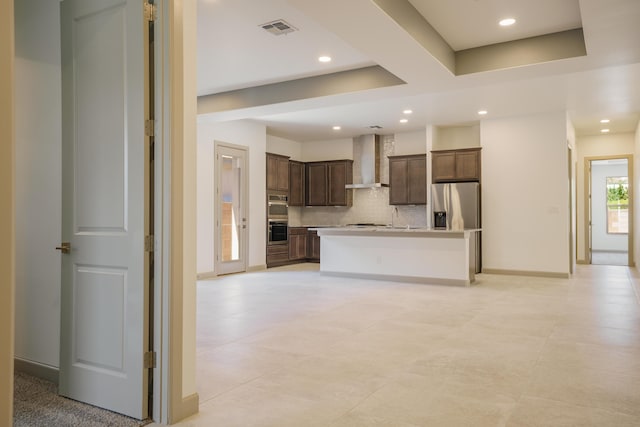 kitchen with tasteful backsplash, sink, a kitchen island with sink, stainless steel appliances, and wall chimney range hood