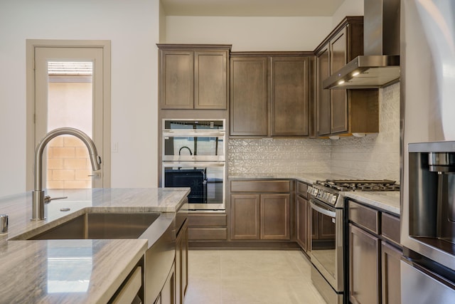 kitchen with tasteful backsplash, light tile patterned floors, stainless steel appliances, light stone countertops, and wall chimney exhaust hood