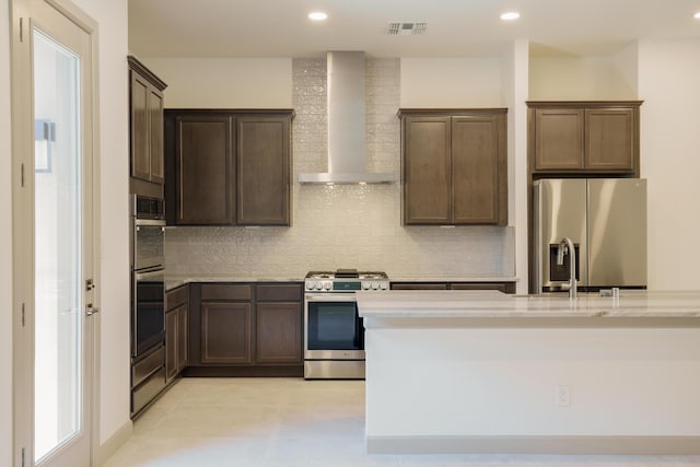 kitchen featuring sink, appliances with stainless steel finishes, dark brown cabinets, tasteful backsplash, and wall chimney exhaust hood