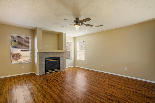 unfurnished living room with a tiled fireplace, a textured ceiling, wood-type flooring, and ceiling fan