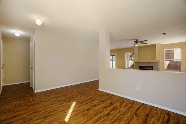 unfurnished living room with dark hardwood / wood-style flooring, a tiled fireplace, a textured ceiling, and ceiling fan