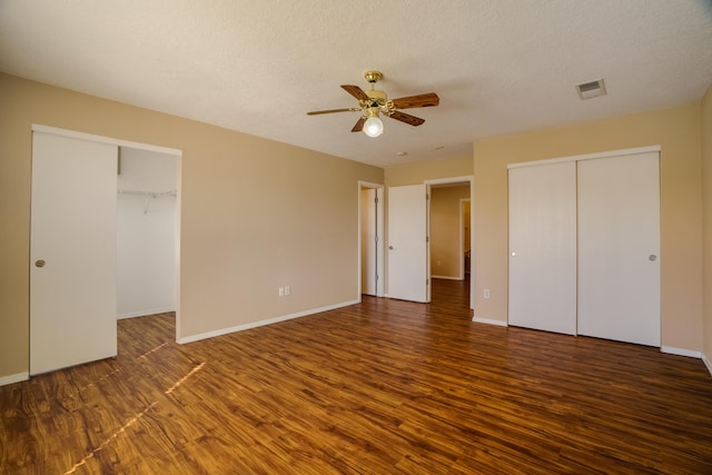 unfurnished bedroom featuring ceiling fan, multiple closets, dark hardwood / wood-style floors, and a textured ceiling