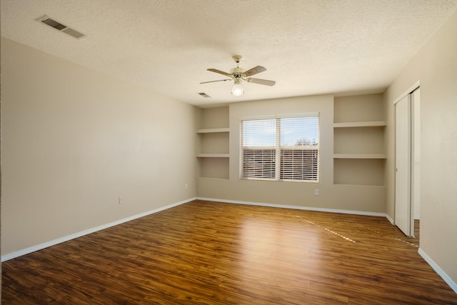 spare room with ceiling fan, built in shelves, dark hardwood / wood-style floors, and a textured ceiling