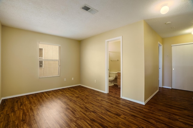 unfurnished bedroom featuring connected bathroom, a textured ceiling, and dark hardwood / wood-style flooring