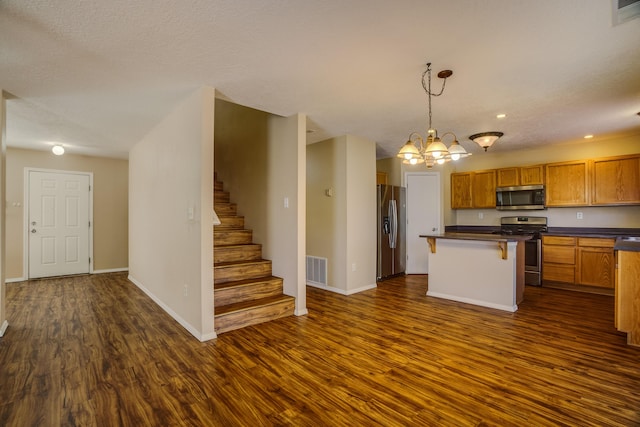 kitchen with dark wood-type flooring, a breakfast bar, appliances with stainless steel finishes, decorative light fixtures, and a chandelier