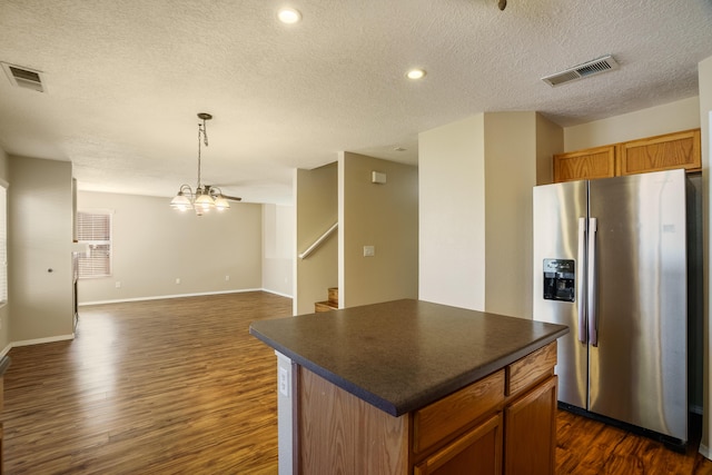 kitchen with dark wood-type flooring, stainless steel fridge, a kitchen island, and a textured ceiling