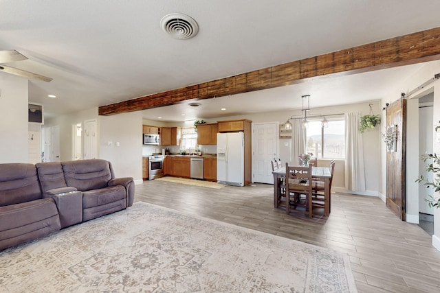 living area with light wood-style floors, a barn door, visible vents, and beam ceiling