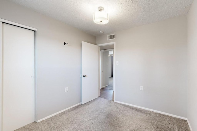 unfurnished bedroom with a closet, visible vents, carpet flooring, a textured ceiling, and baseboards