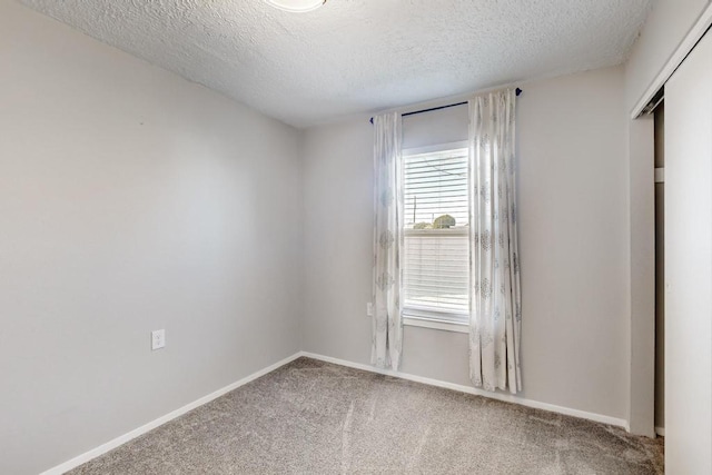 carpeted spare room with a textured ceiling and baseboards