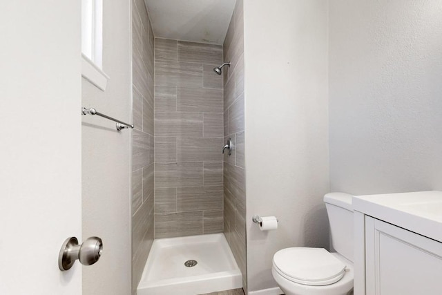 full bath with a tile shower, vanity, and toilet