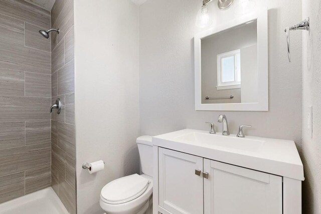 full bathroom with a tile shower, vanity, and toilet