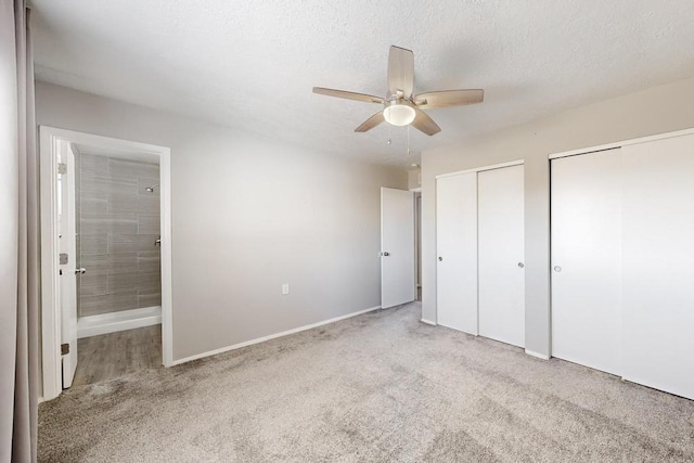 unfurnished bedroom with a textured ceiling, connected bathroom, carpet floors, baseboards, and two closets