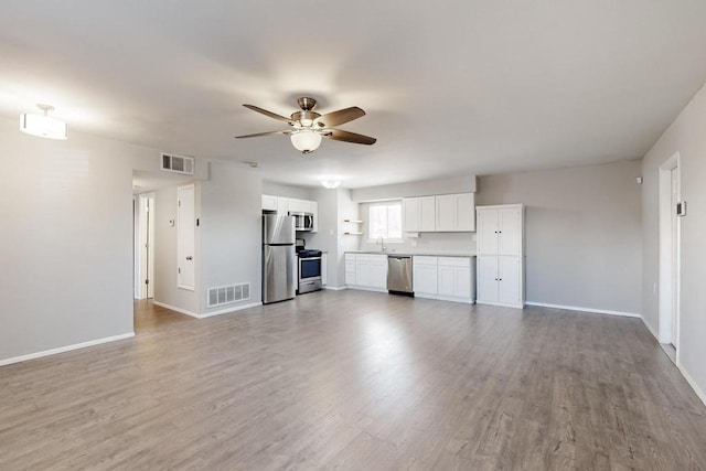 unfurnished living room featuring a ceiling fan, light wood-type flooring, visible vents, and a sink