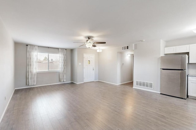 unfurnished living room with light wood-style floors, baseboards, visible vents, and a ceiling fan