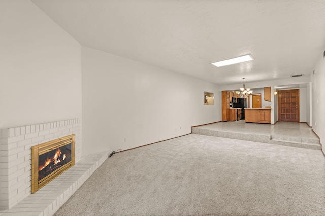 unfurnished living room with a textured ceiling, light carpet, a brick fireplace, and a notable chandelier