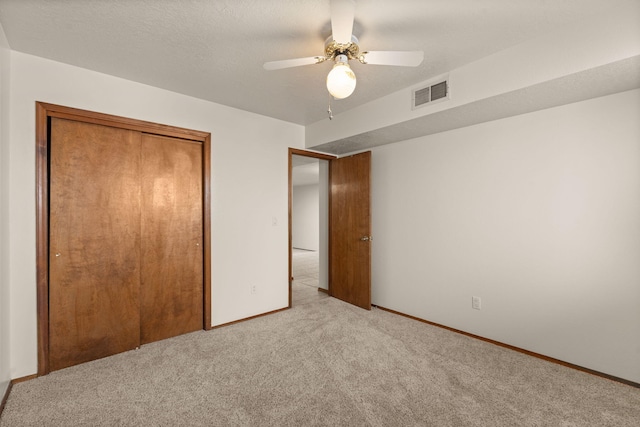 unfurnished bedroom with a textured ceiling, light colored carpet, a closet, and ceiling fan