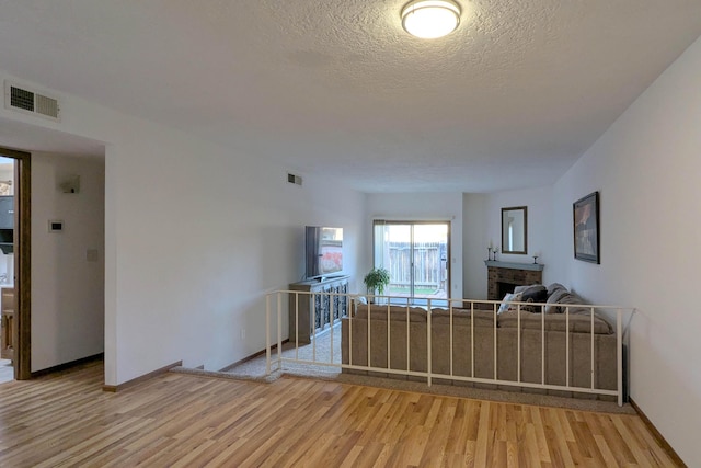 unfurnished living room with a brick fireplace, light hardwood / wood-style flooring, and a textured ceiling