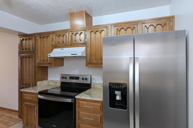 kitchen with light stone counters, appliances with stainless steel finishes, light hardwood / wood-style floors, and a textured ceiling